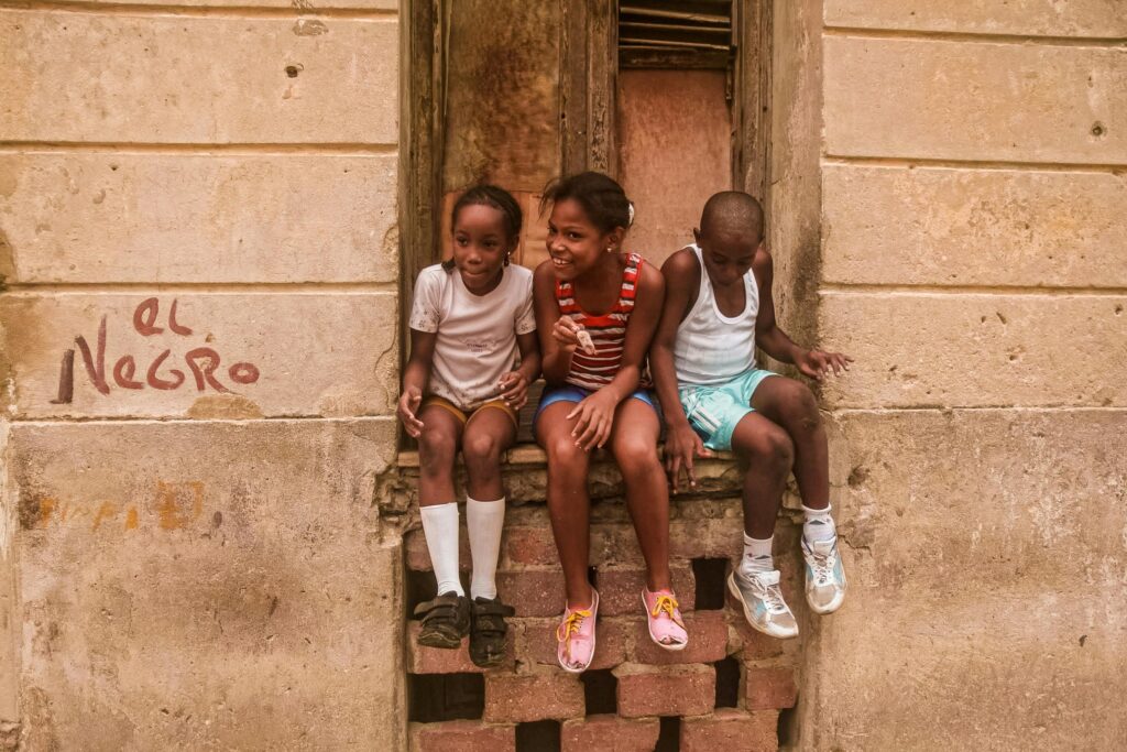 Three children sitting on a window sill in Havana, Cuba, laughing and enjoying a sunny day.